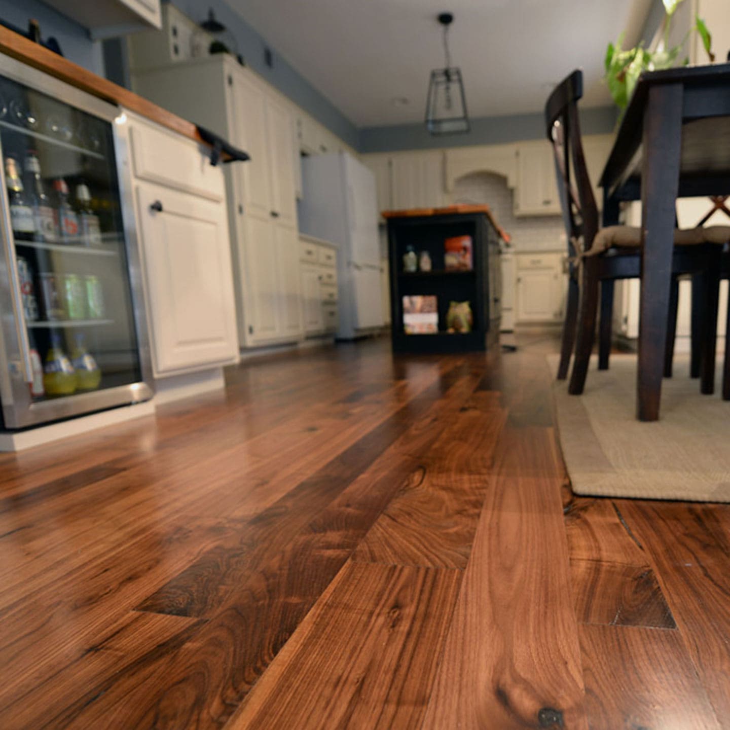 Ambiente de piso de madera sólida, en cocina con una isla de madera, y mesa con sillas del mismo tono sobre tapete color cafe claro | Pisos-de-Madera.mx